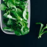 Close-up of fresh green salad leaves in a plastic container on a black background.