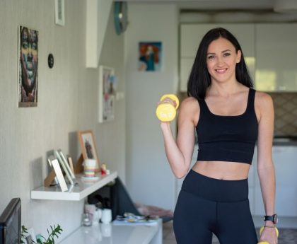 Smiling woman in activewear lifting dumbbells at home for a healthy lifestyle.